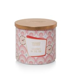 a pink and gold tin with an orange label on the lid that says yankee candle cookie by the fire