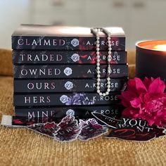 a stack of books sitting next to a candle on top of a wooden table with a pink flower