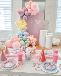 a table set up with balloons, plates and napkins for a unicorn themed birthday party