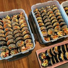 three plastic trays filled with different types of sushi and other foods on top of a wooden table