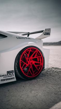 a white sports car with red rims parked on the side of a road next to water