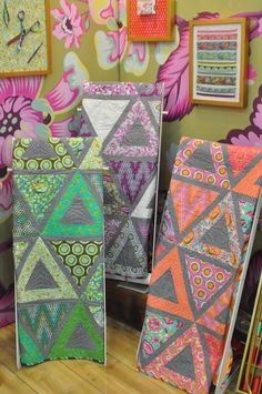 colorful quilts are on display in front of wallpapered pictures and frames with pink flowers