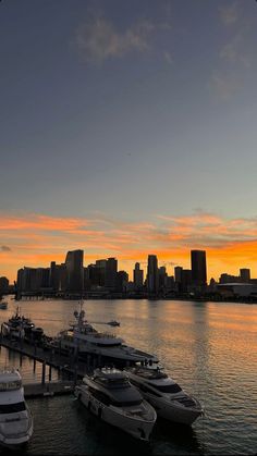 several boats are docked in the water near a large city at sunset or sunrise time