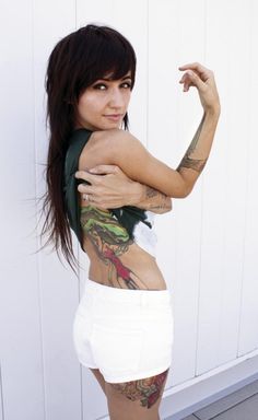 a woman with tattoos on her back posing for the camera while wearing white shorts and a green tank top