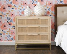 two vases sitting on top of a wooden dresser next to a flower wallpaper