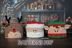 three crocheted christmas mugs with reindeer faces and noses on them, sitting in front of a christmas tree