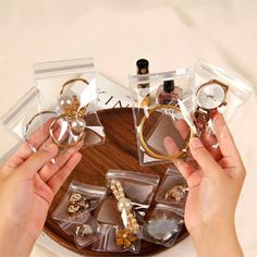 two hands holding rings on top of a wooden tray with clear plastic bags filled with jewelry