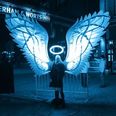 a woman standing in front of a gate with angel wings on it's back