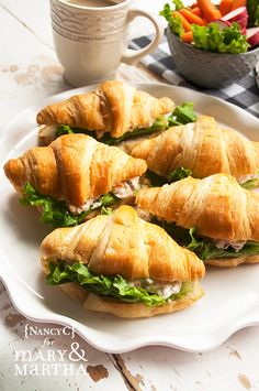 several sandwiches on a white plate next to a bowl of carrots and a cup of coffee