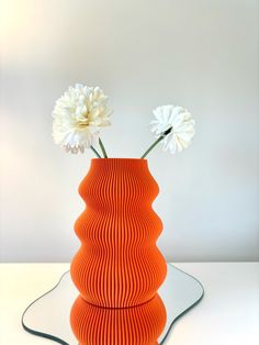 an orange vase with two white flowers in it