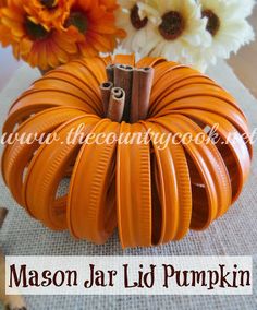 an orange pumpkin sitting on top of a table next to some flowers and cinnamon sticks