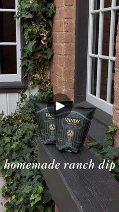 two black bags sitting on top of a wooden bench next to a brick building with ivy growing around it