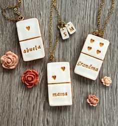 three personalized ceramic necklaces with gold hearts and names on them, sitting on a wooden surface