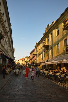 two women walking down the street in front of some buildings with tables and umbrellas