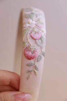 a hand holding a piece of fabric with flowers and leaves embroidered on the inside of it