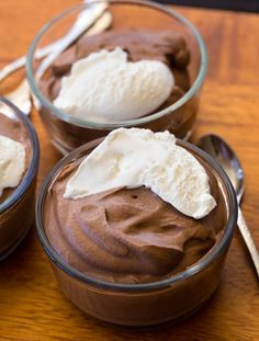 three bowls filled with chocolate pudding and ice cream on top of a wooden table next to two spoons