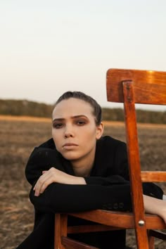 a woman sitting on top of a wooden chair in the middle of an empty field