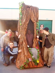 some people are posing for a photo in front of a fake tree stump with flowers and vines on it