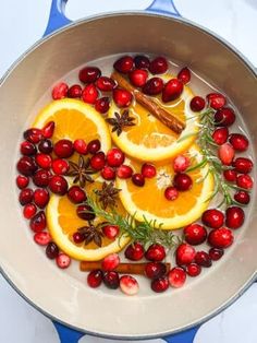 oranges, cinnamon sticks and spices in a pan filled with cranberry sauce