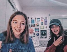 two young women standing next to each other in front of a bedroom with pictures on the wall