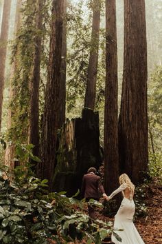 a bride and groom walking through the woods