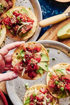 a person holding up a taco with toppings on it and other food in the background