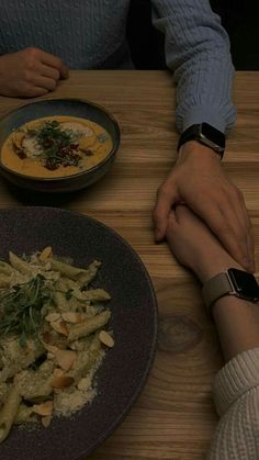 two people sitting at a table with plates of food in front of them, one holding the other's hand