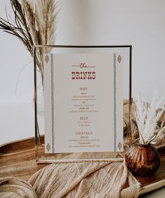 a menu sitting on top of a wooden table next to a vase filled with dry grass