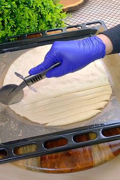 a person in blue gloves is cutting dough on a board with a knife and spatula