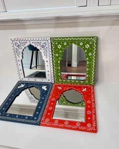 three colorful mirrors sitting on top of a white counter next to a mirror with an ornate frame