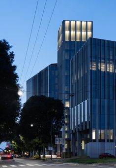 an office building on the corner of a city street at night with traffic passing by