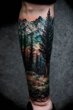 a man's leg with a mountain scene tattoo on his arm and the trees in the foreground