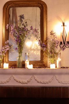 flowers and candles sit on a mantle in front of a mirror