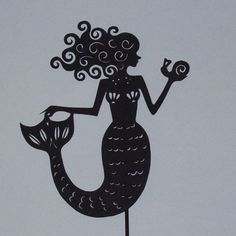 a black silhouette of a mermaid holding a fish on top of a metal stake with swirly hair