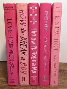 three pink books sitting on top of a wooden table