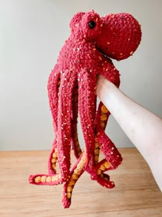 an octopus stuffed animal being held up by someone's hand on a wooden table