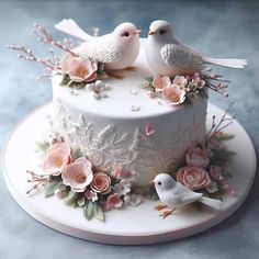 two white birds sitting on top of a cake covered in frosting and pink flowers