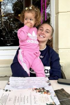 a woman sitting at a table with a child on her lap and papers in front of her