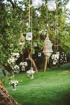 an outdoor wedding with hanging mason jars and flower arrangements on the tree branch for decoration