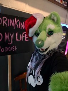 a person wearing a green and white animal mask next to a sign that says drinkin'd my life