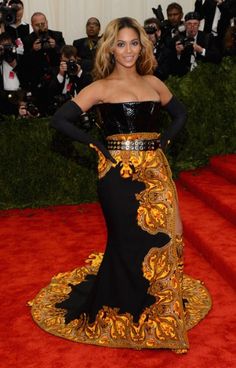 a woman in a black and gold dress standing on a red carpet with cameras around her