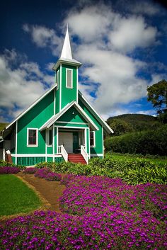 a green and white church surrounded by purple flowers