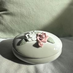 a white box with a pink rose on it sitting on a bed next to a pillow