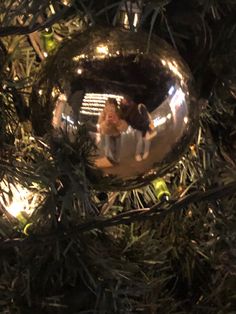 an ornament hanging from a christmas tree with people reflected in the glass ball