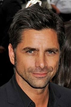 a close up of a person wearing a black shirt and tie with his hair pulled back