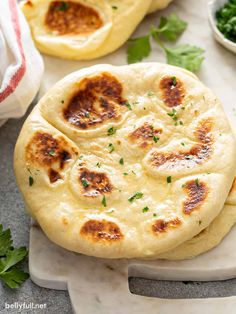 two pita breads sitting on top of a cutting board next to some parsley