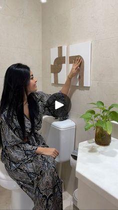 a woman sitting on top of a toilet next to a potted plant in a bathroom