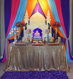 a table topped with cakes and desserts under a colorful drape covered stage curtain