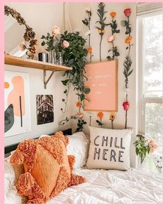 a white bed topped with lots of pillows next to a wall mounted plant and framed pictures