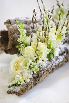 white flowers are arranged in the center of a piece of driftwood that is covered with snow